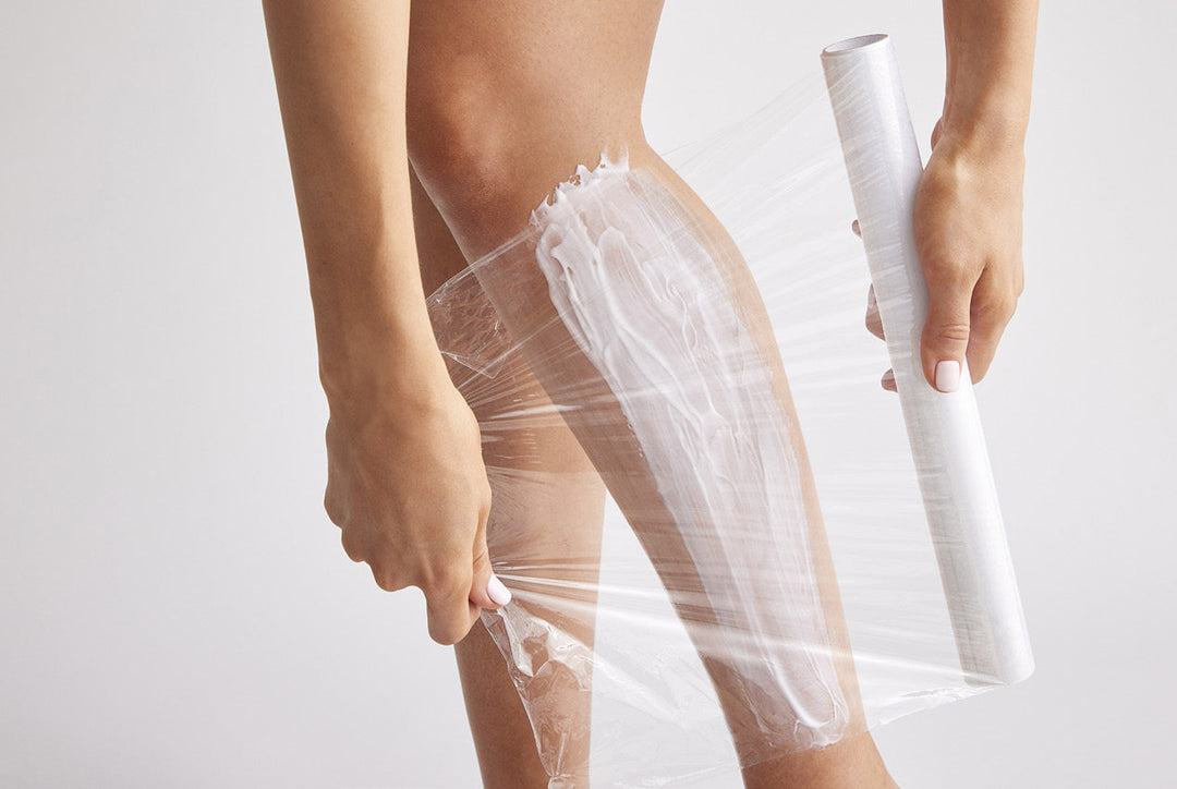 Person using a roll of plastic wrap on their leg against a white background