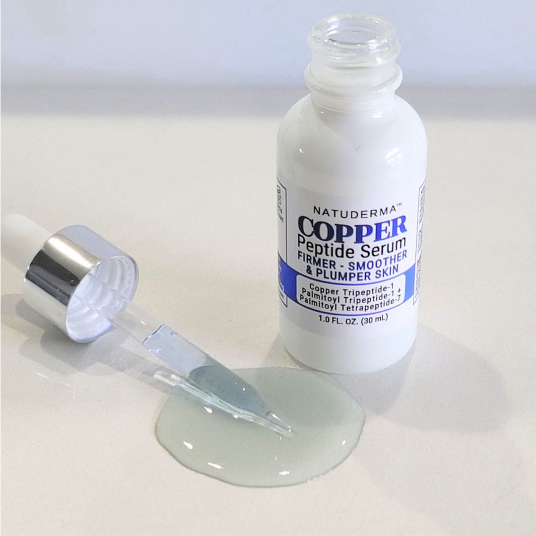 A bottle of Natuderma Copper Peptide Serum stands next to an open dropper with a small pool of pale greenish serum on a light surface.
