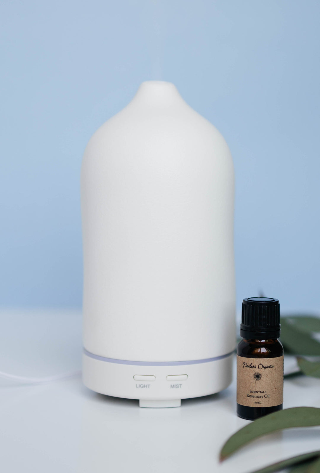 White essential oil diffuser with a bottle of Tula Organics essential oil on a light blue background