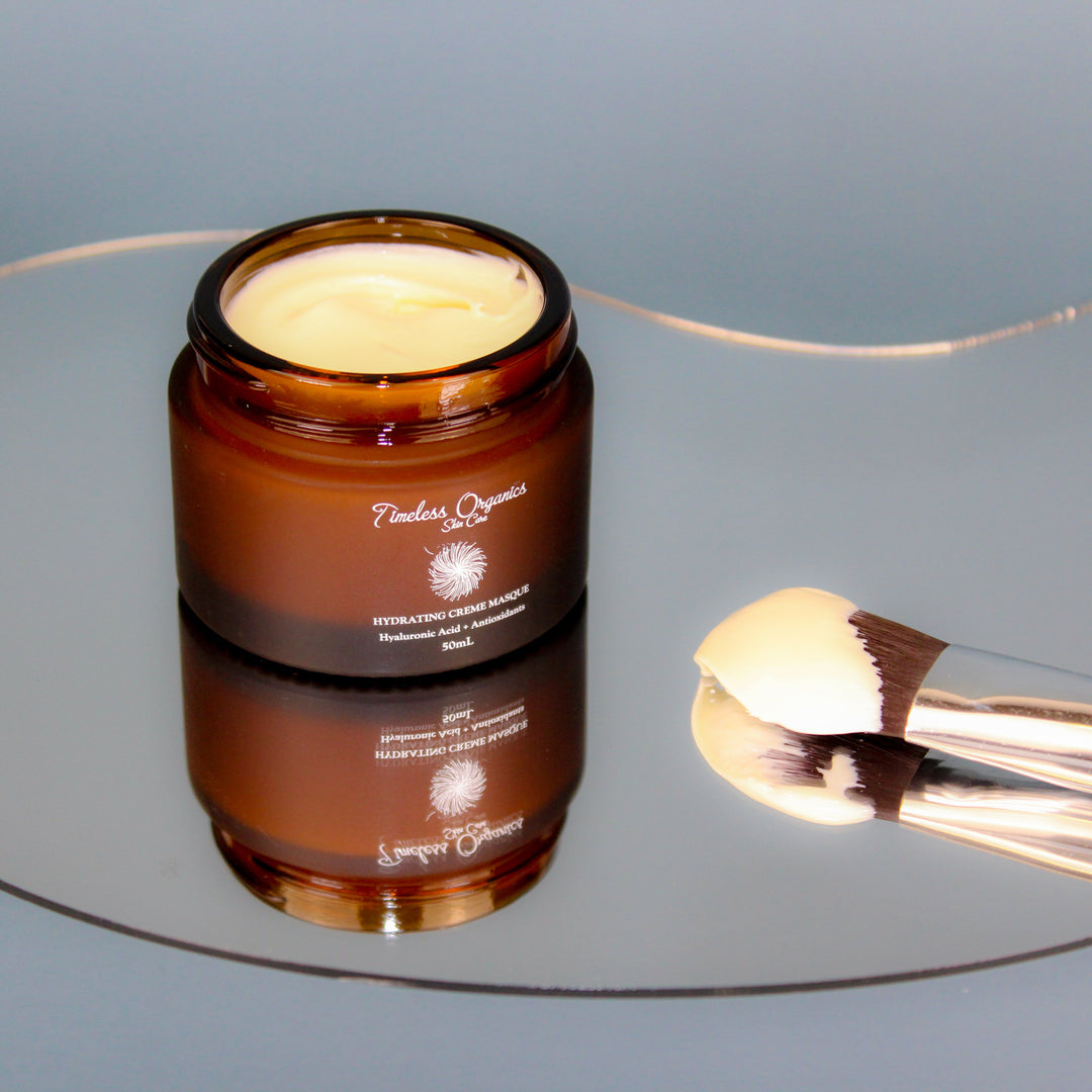 Creamy facial mask on a brown jar with a lid on a reflective surface, accompanied by a makeup brush.