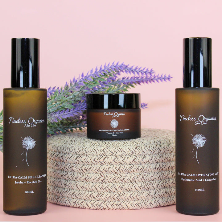 Three bottles of Timeless Organics skincare products on a pink background with lavender.