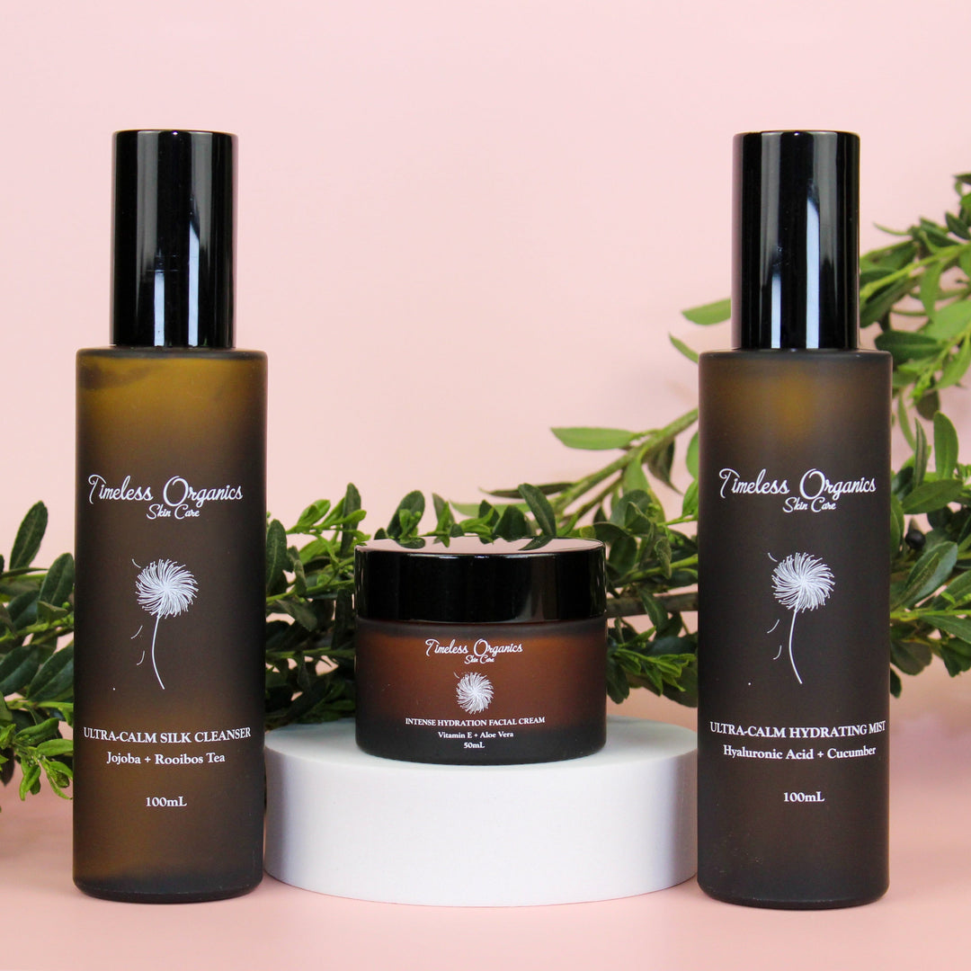 Three Timeless Organics skincare products on a pink background with green leaves.