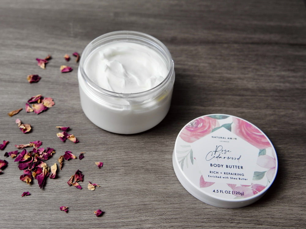 Body butter jar with lid on a wooden surface surrounded by rose petals