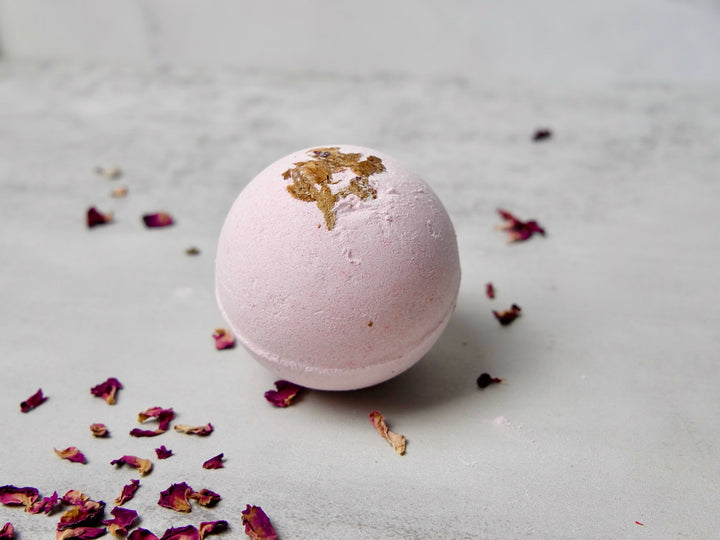 Pink bath bomb with gold leaf on a gray surface with dried flowers