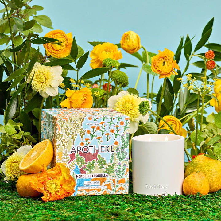 Apotheké candle and packaging with flowers and oranges on a grassy background
