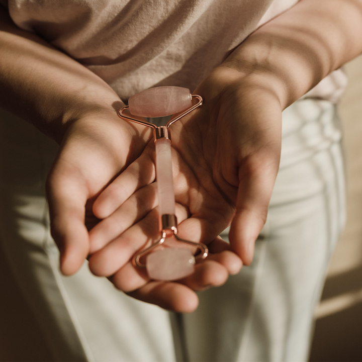 Person holding a rose gold roller with pink stone in their hands