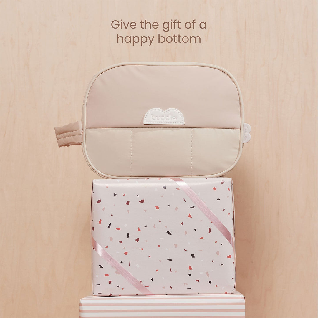 Beige pouch on a gift box with text 'Give the gift of a happy bottom' on a wooden surface