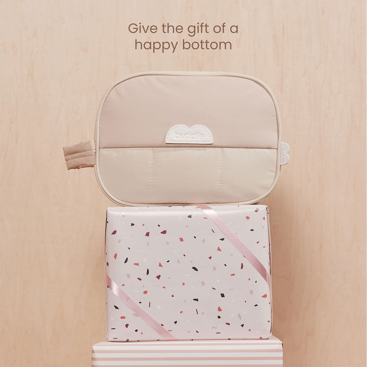 Beige pouch on a gift box with text 'Give the gift of a happy bottom' on a wooden surface