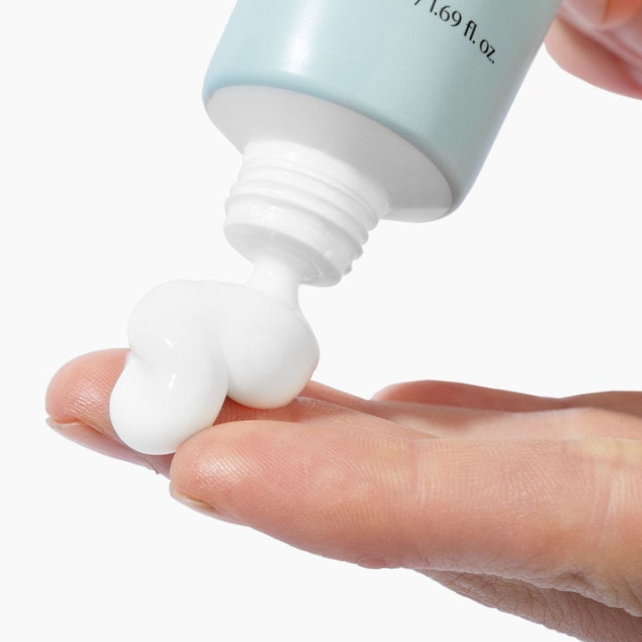 Hand holding a tube of Korean cream with a close-up of the cream being squeezed out.