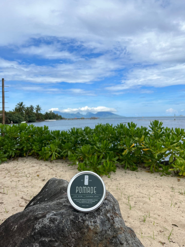 Pomade container on a rock with a beach and mountains in the background