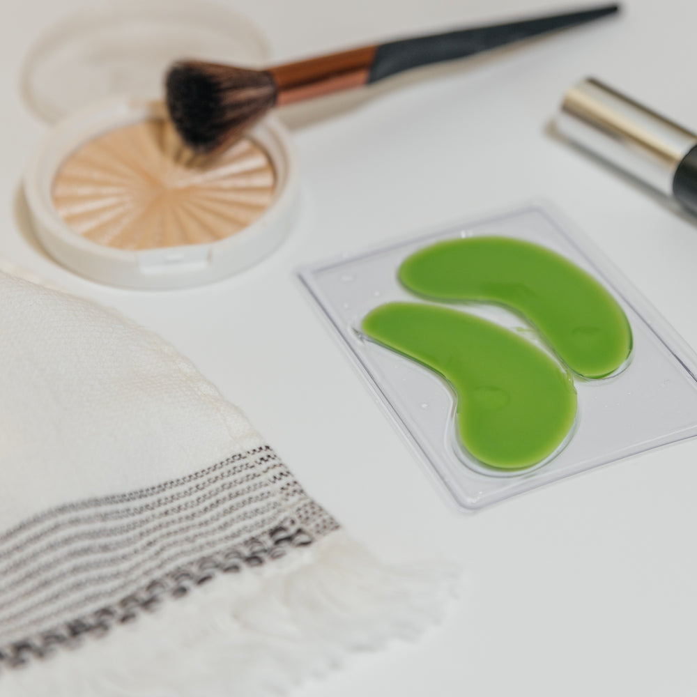 Eye mask - Green eye patches on a white surface with makeup tools.