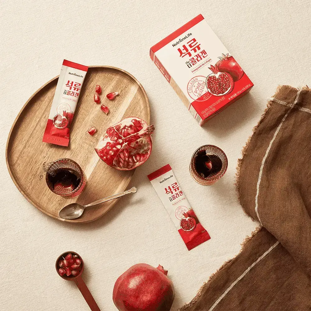 Pomegranate products including a box, packets, and fresh pomegranates on a wooden tray.