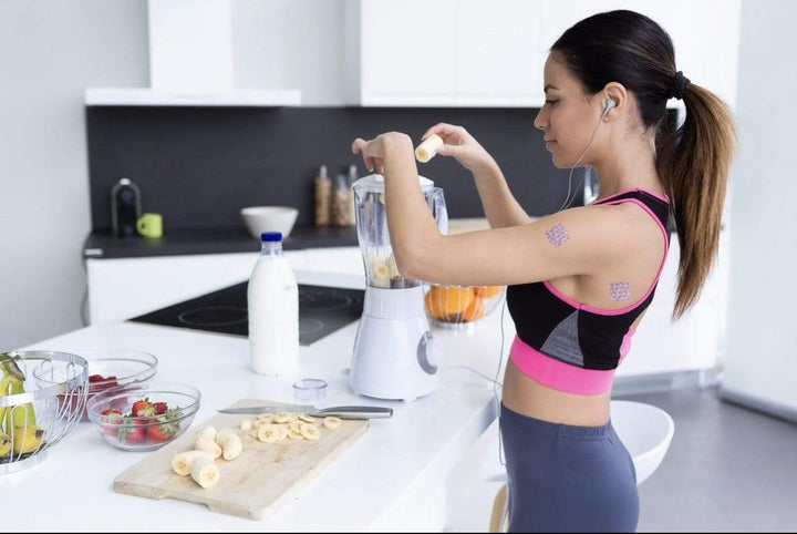 Woman in athletic wear preparing food in a kitchen with energy patches on her arm